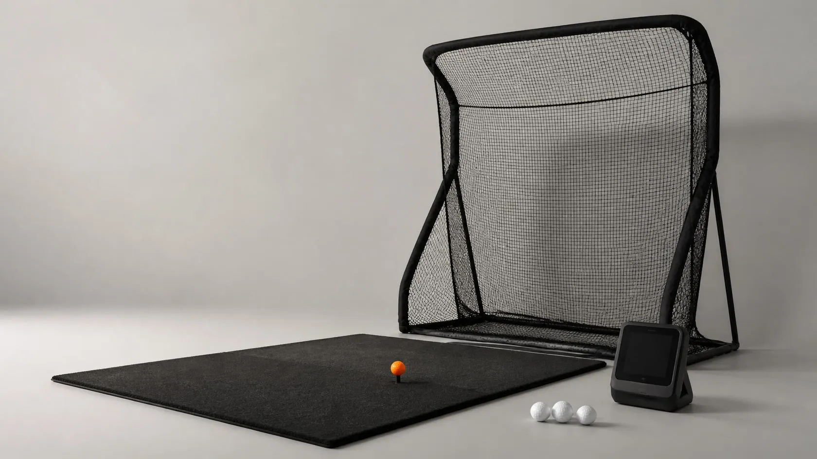 Kompakt golfsimulator-hörna: slagmatta, träningsnät, launch monitor med avstängd skärm och golfbollar, varav en orange på peg