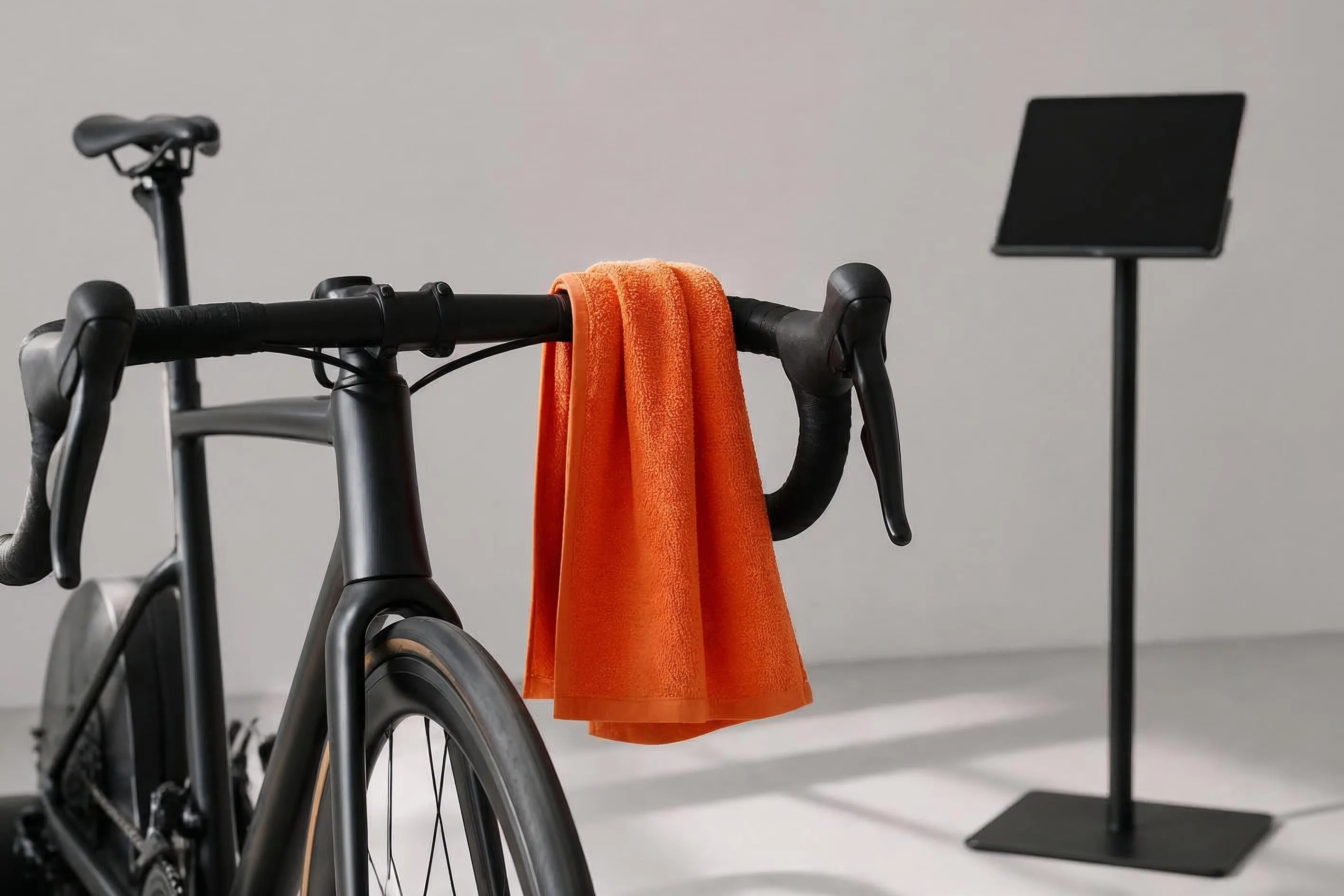 Racerstyre med en orange handduk draperad över, framför en avstängd surfplatta på stativ
